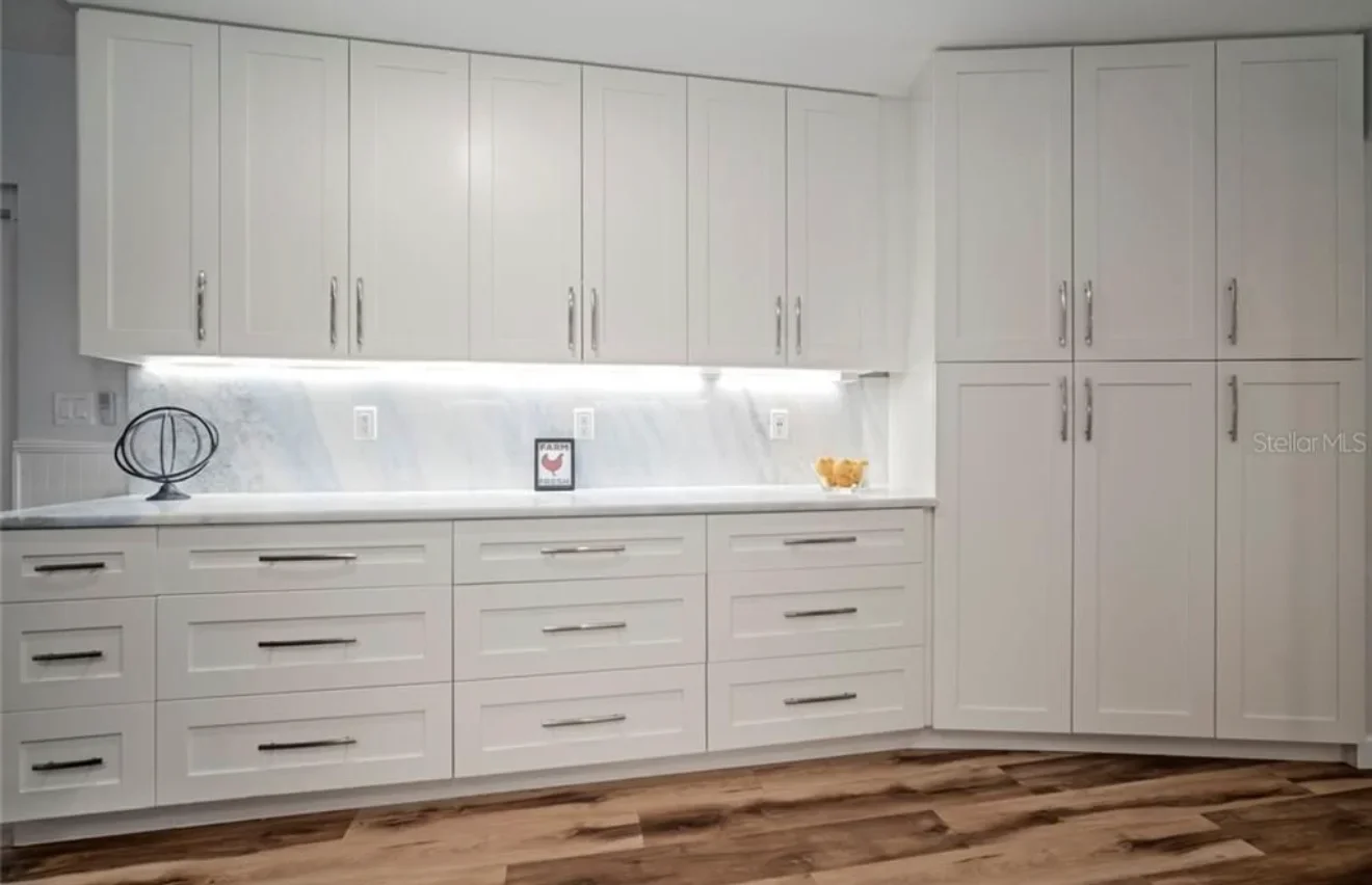 Modern white kitchen with custom cabinetry, LED lighting, and marble backsplash